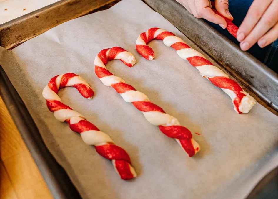 Unbaked candy cane cookies made from red and white twisted dough, placed on a parchment-lined baking sheet