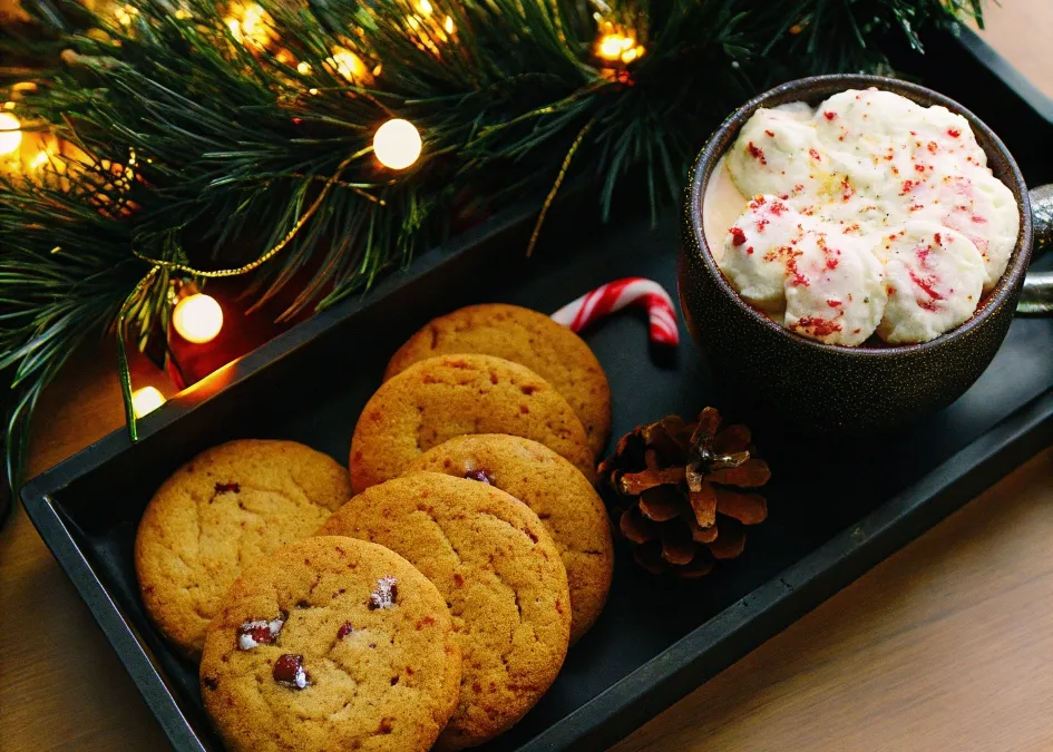 A holiday platter of candy cane cookies with a cup of hot cocoa, surrounded by festive Christmas decorations.