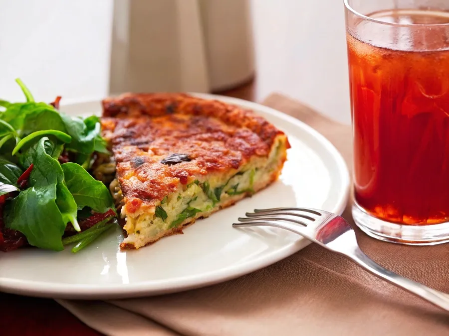 A slice of zucchini pie served with a fresh salad and iced herbal tea