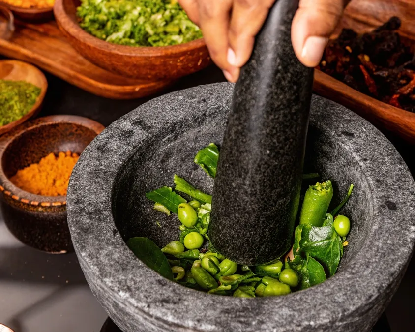 Fresh green sundakai being crushed on a traditional stone grinder for sambar preparation.