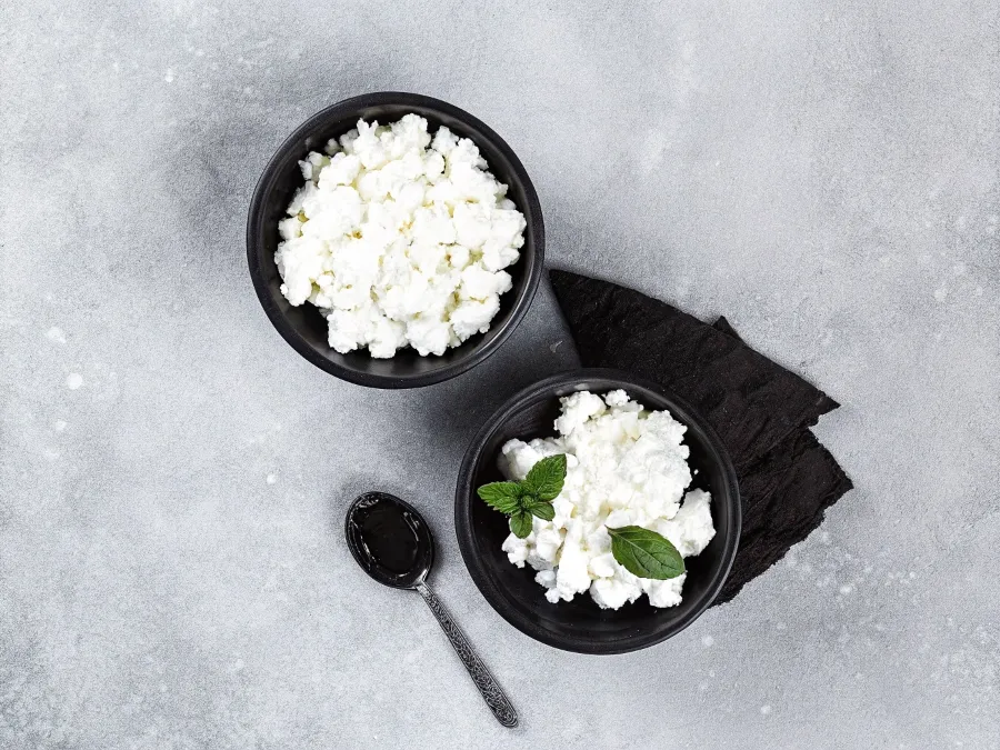 A side-by-side comparison of creamy ricotta cheese and chunky cottage cheese in bowls with fresh basil.