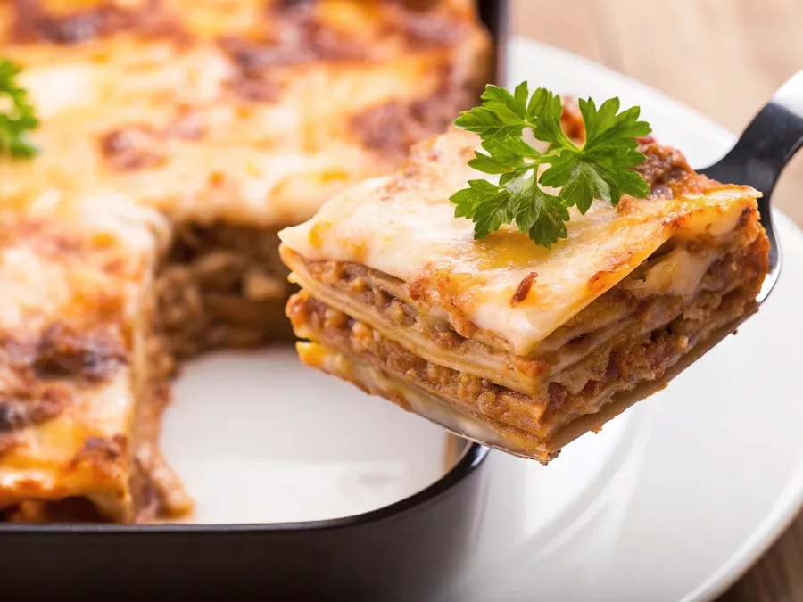 A slice of lasagna with creamy béchamel sauce being served.