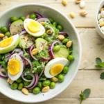 Colorful edamame egg salad with fresh greens, eggs, and sesame seeds in a white bowl.